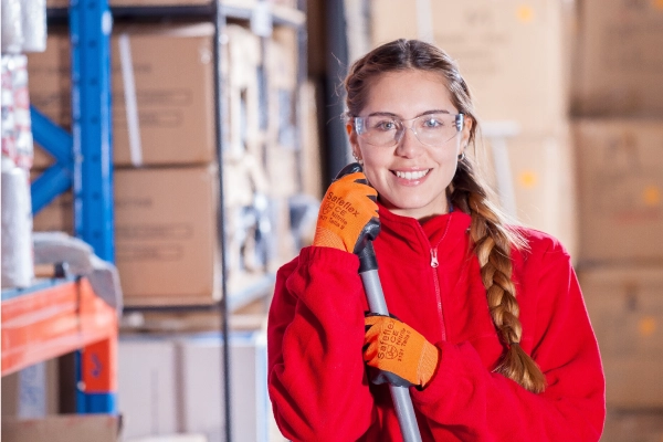 Lady wearing safety glasses, gloves and a fleece, holding a brush