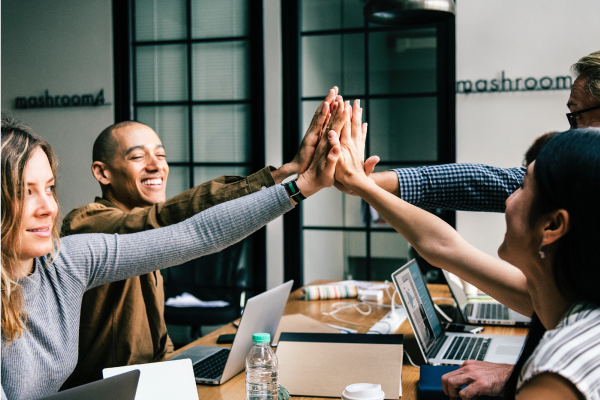 Team hi five across desk with computers on