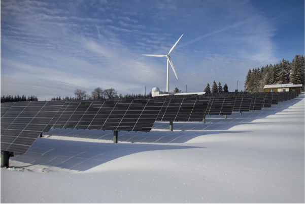 Wind turbine behind solar farm with ground covered in snow